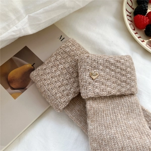 Detail of beige knit winter gloves with golden heart buckle and soft texture on white cloth