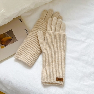 Close-up of beige knit gloves with long ribbed cuffs and small leather logo detail
