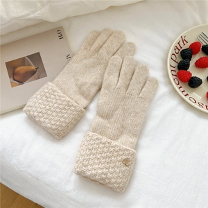 Detail of oat-beige knitted gloves featuring heart metal charm and textured cuff design