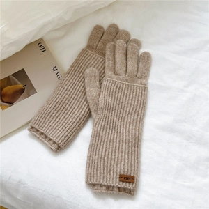 Detail of beige knit gloves with long cuffs and brown leather patch on white linen