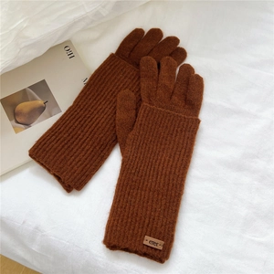 Detail of dark brown knit gloves with ribbed texture and decorative leather logo patch