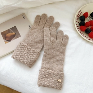 Detail of khaki thick knit gloves with folded cuffs and heart logo on soft fabric