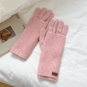 Detail of pink ribbed knit gloves featuring a leather brand tag on a cozy white background
