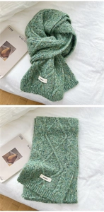 Detail of green cable-knit wool scarf with textured weave and brand label on folded fabric