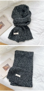 Detailed knit texture of a chunky dark grey winter scarf with white woven brand label