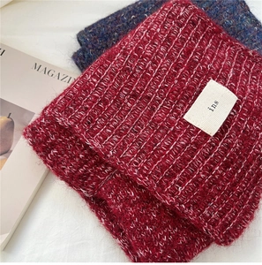 Detail of burgundy ribbed knit scarf featuring white woven label on soft textured fabric