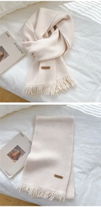 Close-up of cream knit scarf featuring soft fringe and brown leather Hand Made label