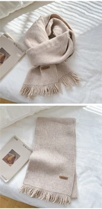 Detailed view of beige knitted scarf featuring long fringe and a brown Hand Made label
