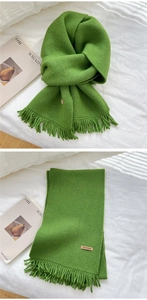 Detail of green knit scarf featuring tassel edges and a brown 'Hand Made' leather label