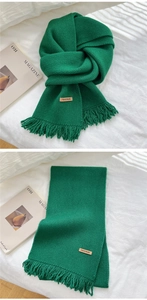 Close-up of dark green knitted scarf with handmade leather label and tassel fringe details