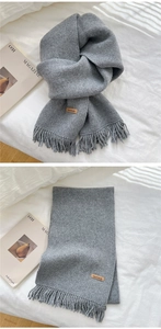 Detail of grey knitted scarf showing handmade leather tag and soft fringe textures