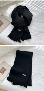 Detail view of black knit scarf featuring tassel fringe and handmade leather label