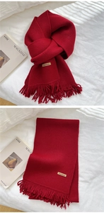 Close-up of deep red knitted scarf with tassels and a stitched Hand Made leather tag