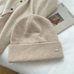Detailed knit texture of beige beanie featuring a small oval silver metal logo tag
