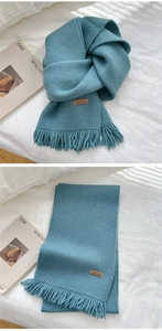 Detail of teal knitted scarf with long tassels and brown handmade leather label