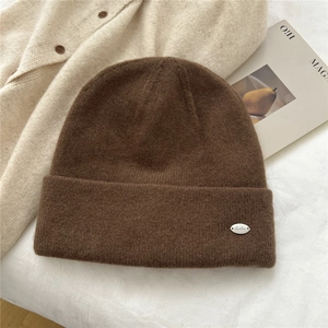 Detail of coffee brown knit beanie with silver logo plate on soft textured fabric