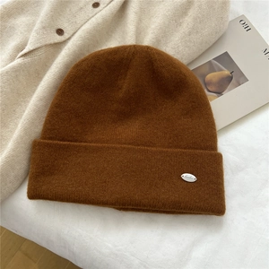 Close-up of dark brown knit beanie texture with a decorative silver metal brand plate