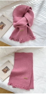 Detail of pink knitted scarf featuring fringe ends and a brown Hand Made leather label
