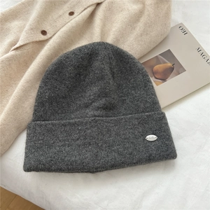 Detail of dark grey knit beanie featuring a silver oval metal logo on soft wool fabric