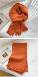 Detail of bright orange knitted scarf with fringe and Hand Made leather label