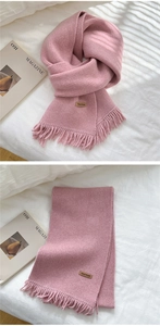 Detail of pink knitted scarf featuring decorative tassels and a handmade leather tag