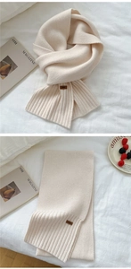 Detail of soft cream knitted scarf featuring ribbed edges and a brown leather logo tag