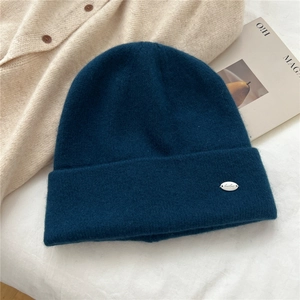 Close-up of dark teal knit beanie with silver metal emblem on soft textured wool