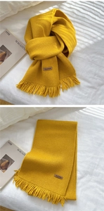 Detail of yellow knitted scarf featuring short tassels and a Hand Made leather label
