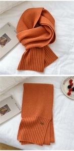 Detail of bright orange knitted scarf with ribbed edges and small leather decorative tag