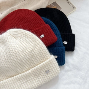 Detailed view of ribbed knit beanies in cream, burgundy, navy and black with metal logo