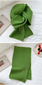Detailed knit texture of green winter scarf with stitched leather logo tag and ribbed edge