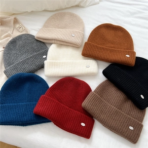 Minimalist knit beanie hats in multiple colors stacked on white soft bedding decor
