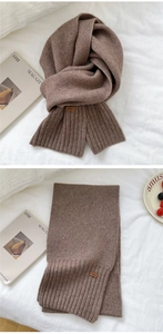 Detail of soft brown knitted winter scarf featuring ribbed cuffs and branded leather tag