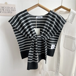 Détail du châle en tricot rayé noir et blanc avec étiquette de marque sur chemise blanche