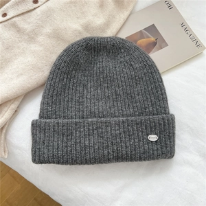 Close-up of a dark grey ribbed knit beanie featuring a metallic brand logo on a soft fabric