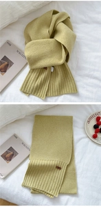 Detail of yellow knit scarf showing soft wool texture and ribbed edge with brown label