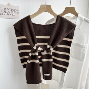 Détail macro du châle en tricot de laine rayé marron et crème sur un cintre