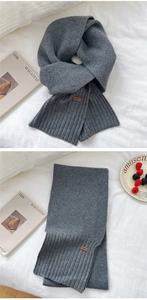 Close-up of dark grey knitted scarf with ribbed edges and decorative leather patch