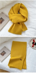 Detail of ginger yellow knitted scarf featuring ribbed edges and a small leather tag