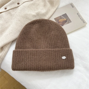 Detailed texture of dark brown ribbed knit beanie with small oval metal logo plate