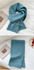 Detail of blue knitted scarf with ribbed edge and elegant brown leather logo tag