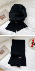 Close-up of black knitted winter scarf with ribbed edges and small leather brand tag