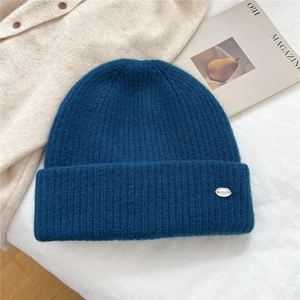 Close-up of dark blue ribbed knit beanie with silver metal logo tag on folded brim