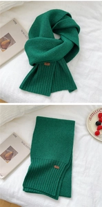 Detailed knit texture of a dark green winter scarf with an embossed decorative leather tag