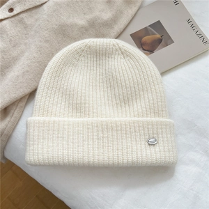 Detailed shot of cream knitted beanie with a silver metal plate on folded cuff