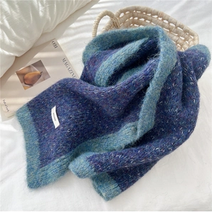 Detail of blue-purple knit scarf with light blue trim and brand tag on white sheets