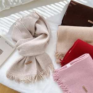 Thick knit fringe scarves in five warm colors on white bedding, minimalist winter style