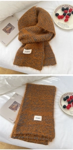 Detail of caramel knit scarf with blue stripes and brand label on cozy white bedding