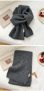 Close-up of dark grey chunky knit scarf texture with a woven brand tag on white fabric