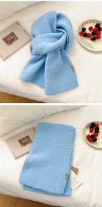 Detail of sky blue thick knit scarf with leather logo label and warm texture